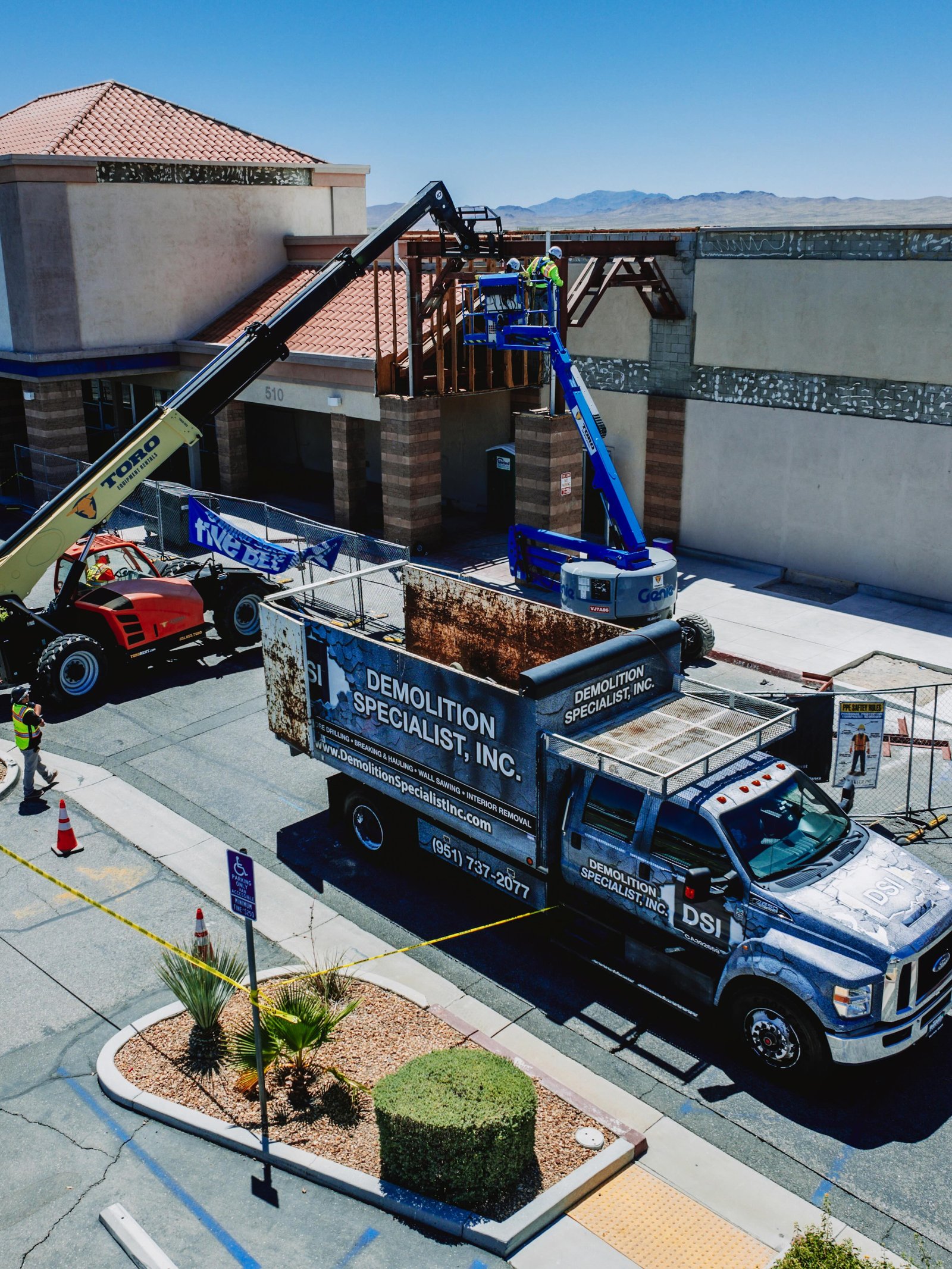 Aerial view of DSI Demolition Specialist service truck parked with boom lift and crew working at elevation on commercial building