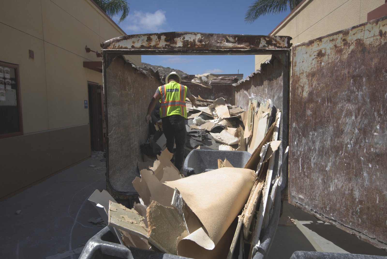 DSI laborer loading interior demolition debris into roll-off container from inside
